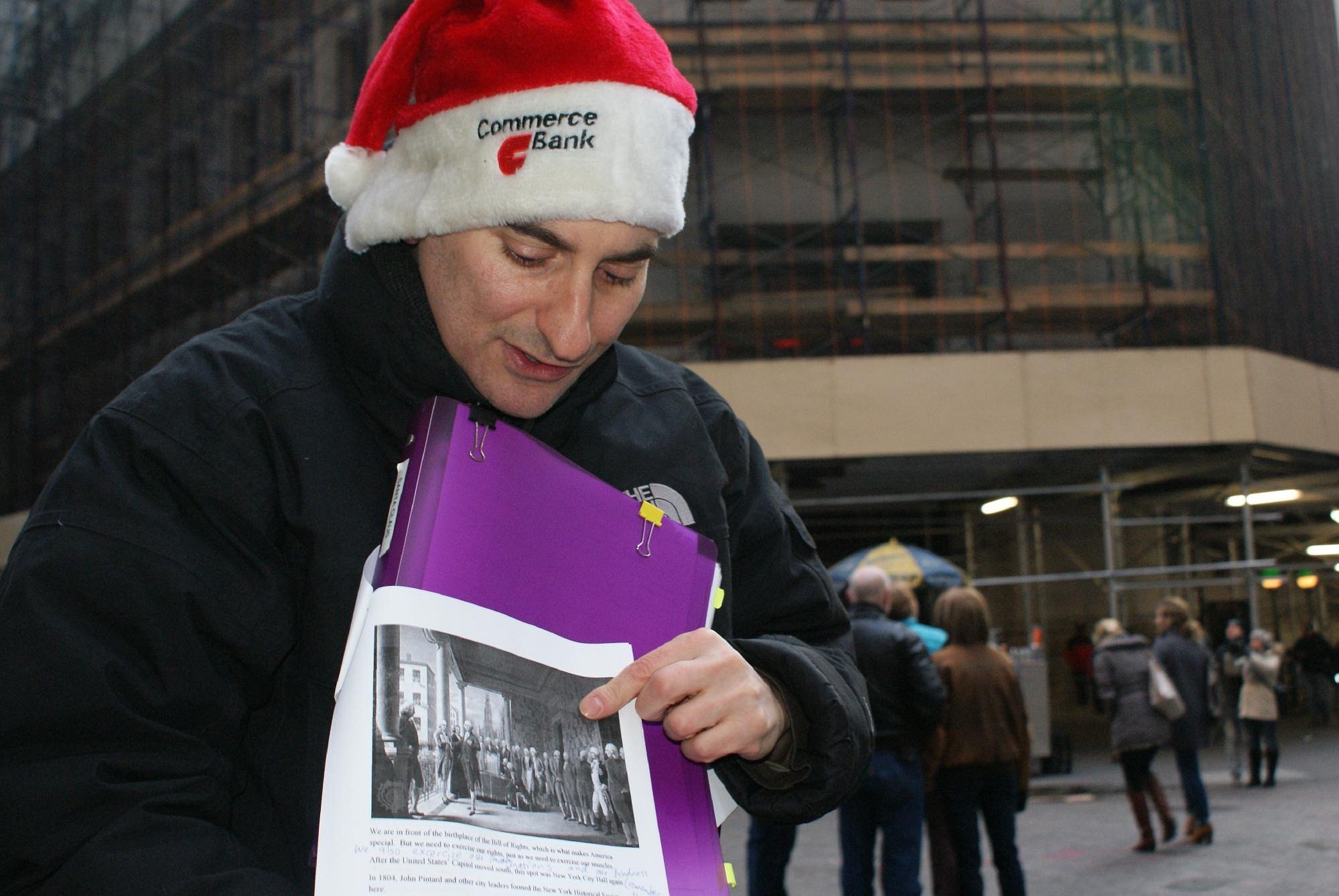 Jared in a Santa hat holding a tour binder in Lower Manhattan during the holidays