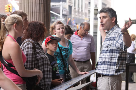 Jared holding up a dollar bill while teaching a group of students on a Midtown sidewalk